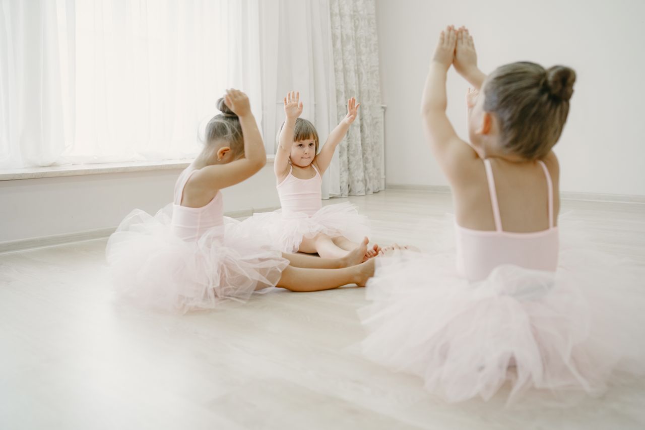 Three young ballet dancers in a dance class practicing poses, wearing tutus.